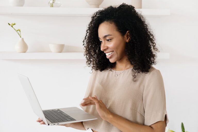 Happy African American woman standing in neat home office holding a laptop