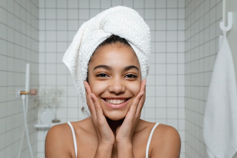 Attractive girl doing skin care in white bathroom while touching her face and smiling